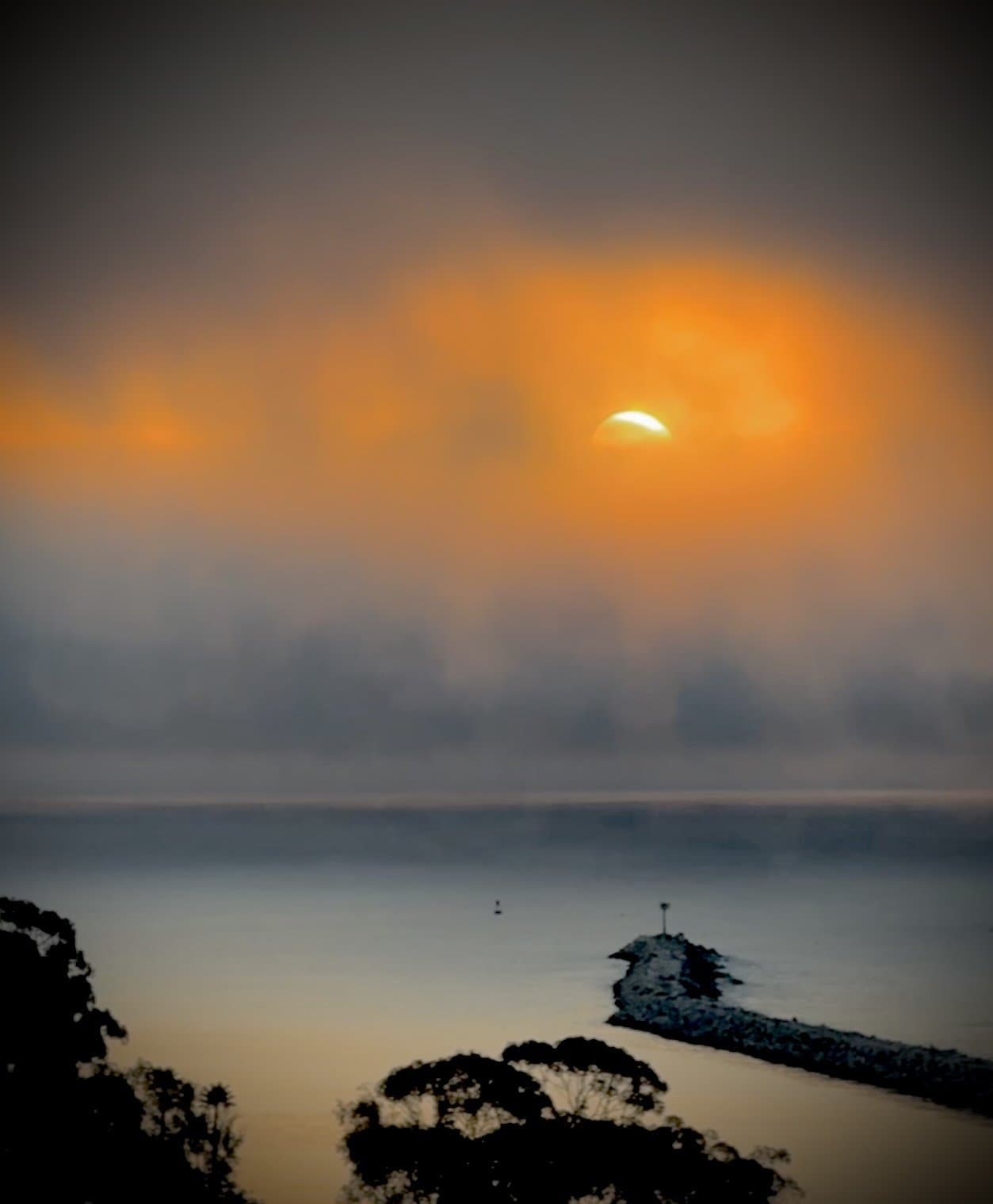 Sun burning through marine-layer fog over a harbor jetty at dawn