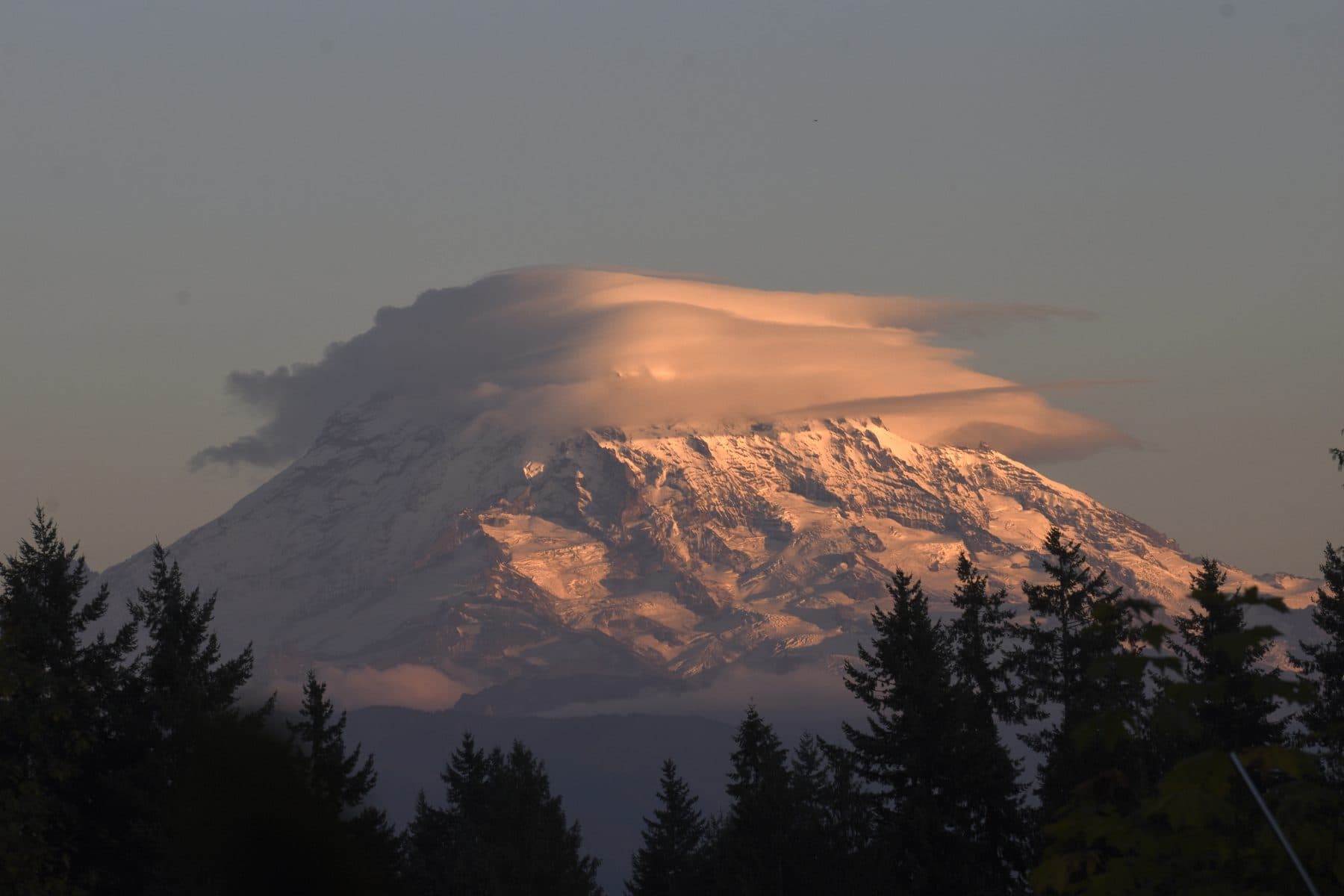 A lenticular cloud capping a snow-covered mountain at dusk
