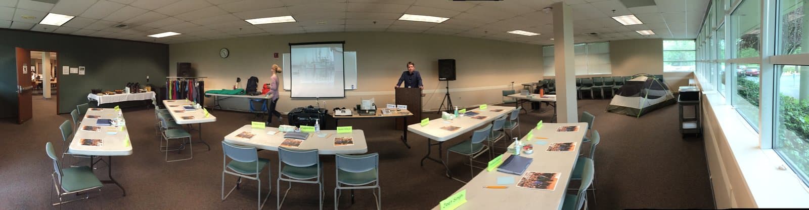 A training room set up with tables, laptops and a projector screen before a class